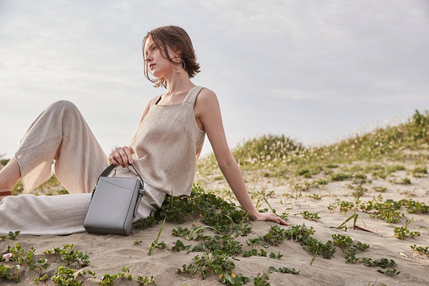 Eine stilvoll gekleidete, umweltbewusste Frau trägt eine nachhaltige Ledertasche von BONAVENTURA am Strand. 