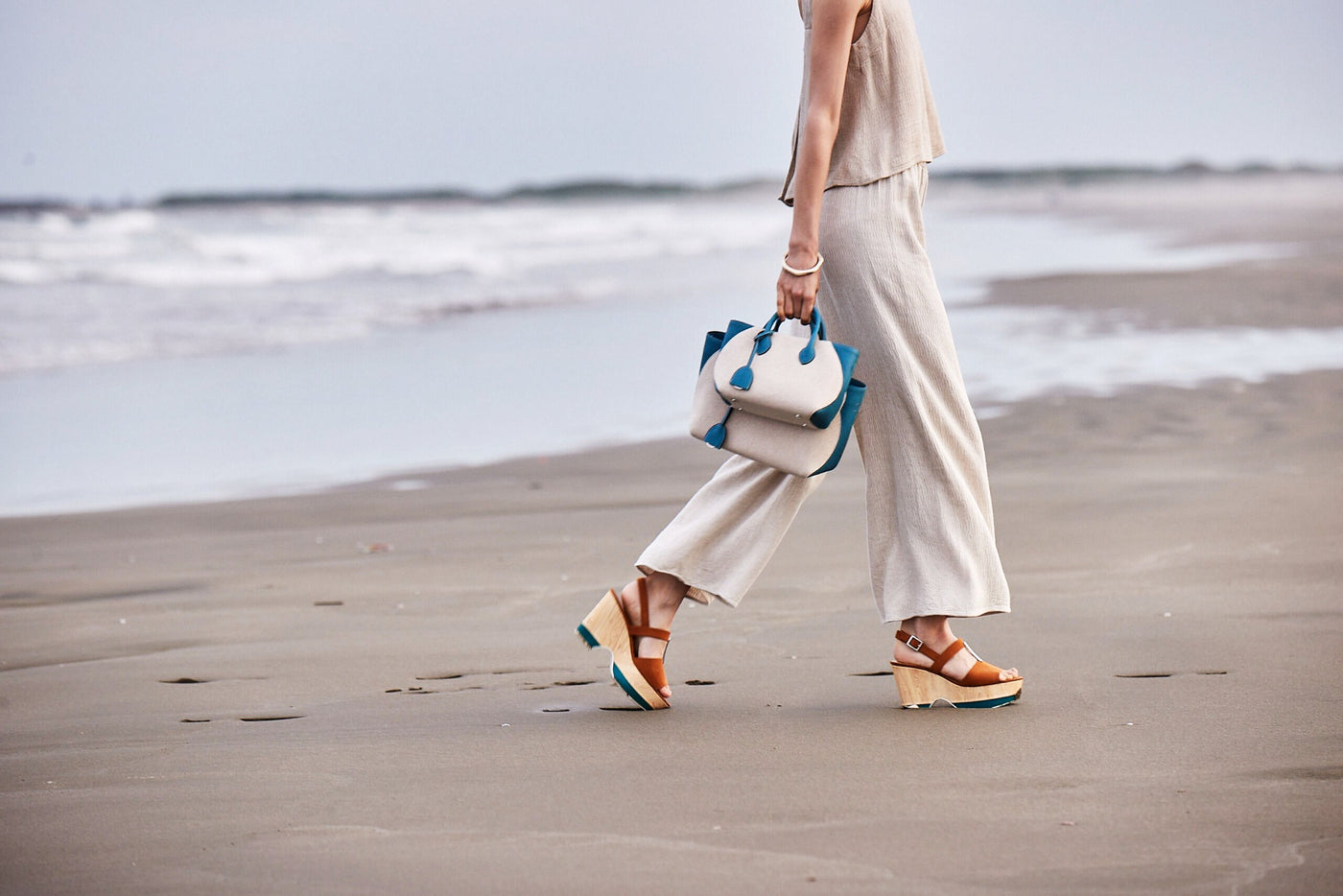 Frau mit eleganter Strandtasche spaziert am sonnigen Strand.